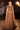 Ladivine full-length formal gown in bronze, featuring a beaded cross-front bodice, boat neckline, and dramatic floor-length cape sleeves, suitable for galas.