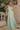 Ladivine chiffon maxi gown in sage green, featuring a draped one-shoulder neckline with a flowing sash detail, ideal for bridesmaids or formal spring events.
