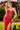 Woman in a red strapless dress with a high slit standing outdoors.